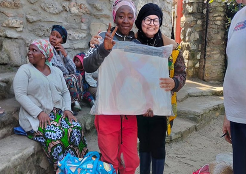 Community members and a volunteer holding up a hand-drawn poster at an outreach day