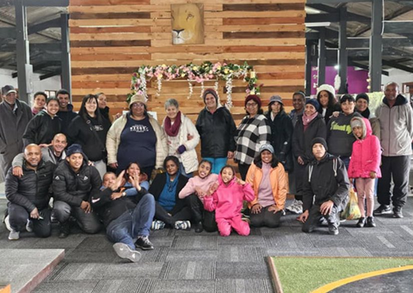 Parents, staff and children gathered in front of a decorated wooden wall at an ECD event